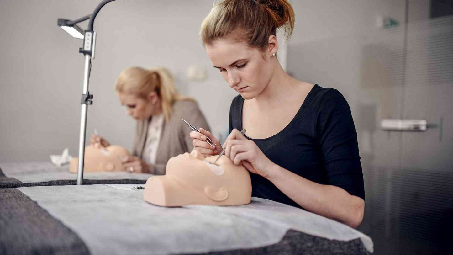 Mokinės atlieka blakstienų priauginimą kursų metu ant specialių manekenų