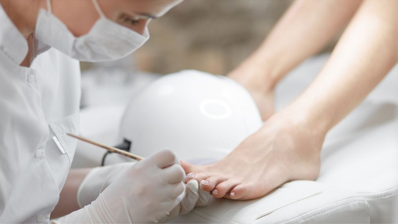 Pedikiūro meistrė su kauke ir pirštinėmis atlieka pedikiūrą klientei Silart akademijos pedikiūro kursuose